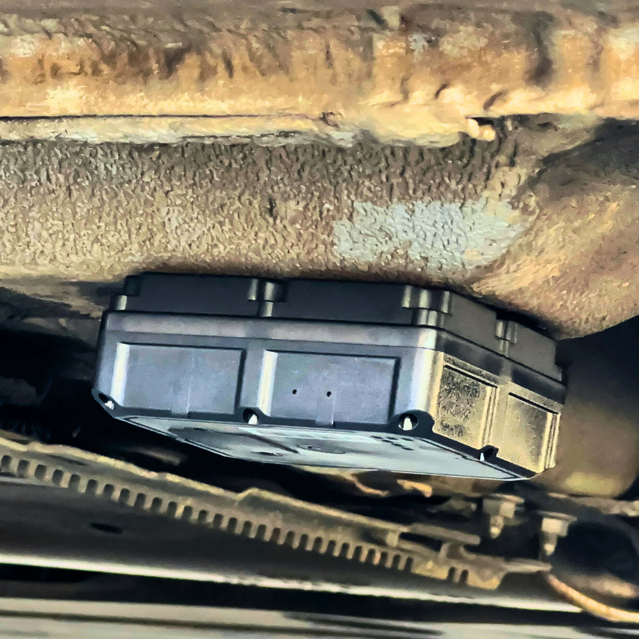 Black rectangular GPS tracker attached to the underside of a vehicle, shown close-up against a metal surface.