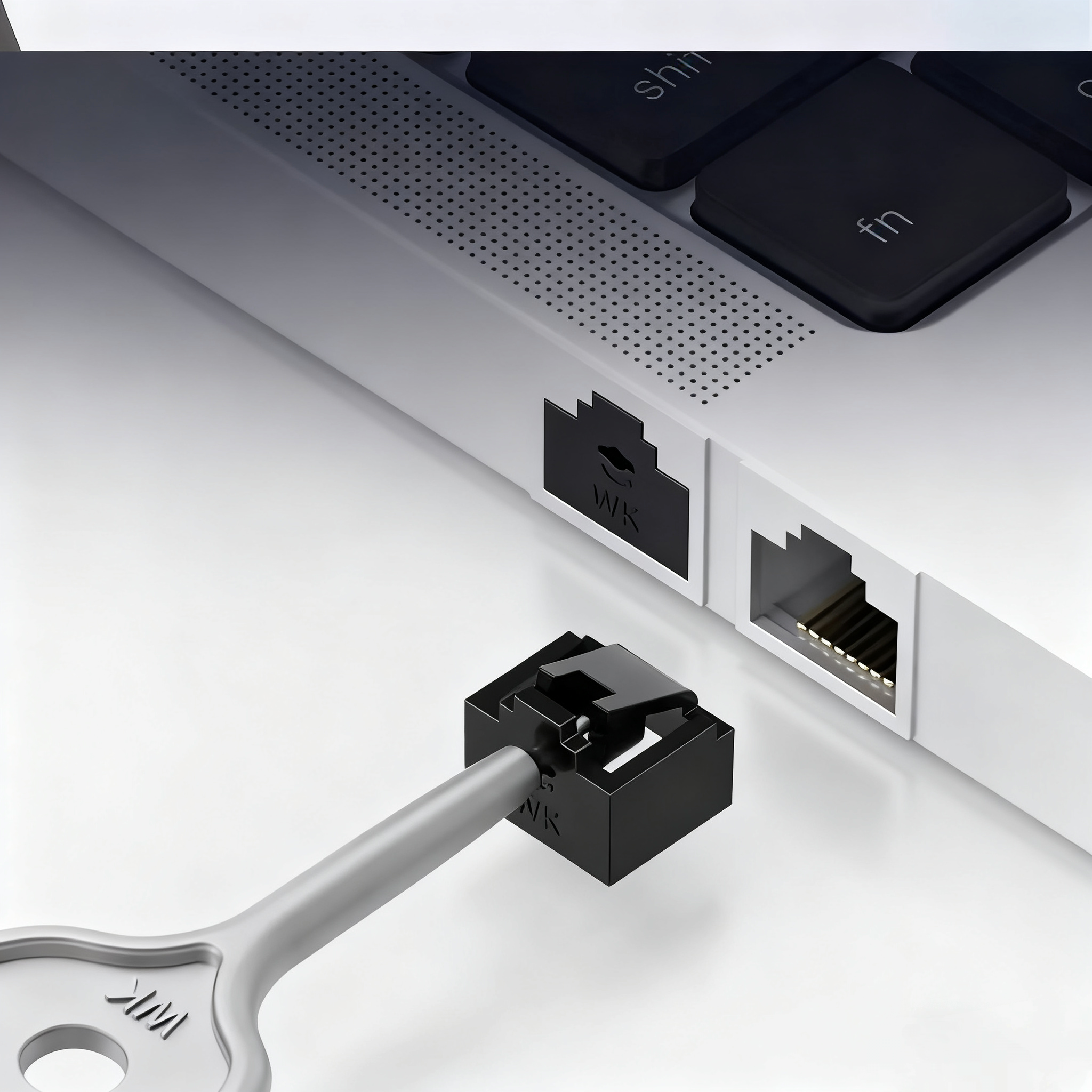 Single black RJ45 port blocker with silver key beside a white laptop's Ethernet port and keyboard