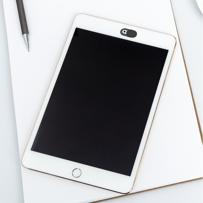 A white tablet with a black webcam cover slider attached over the front camera, on a white desk.